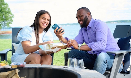 couple looking at smart phone with wine by fire pit