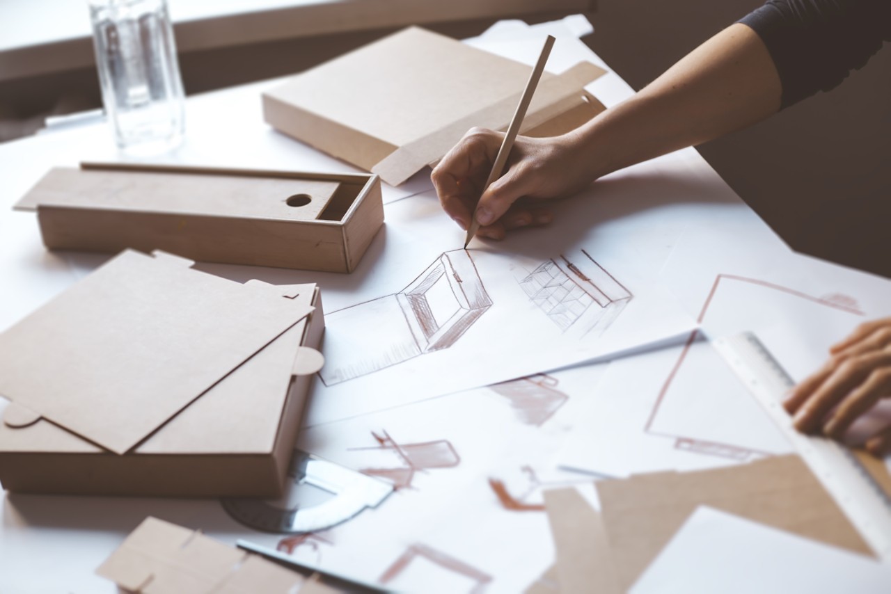 Designer draws a mockup for crafting cardboard box. Development of packaging design sketch. 