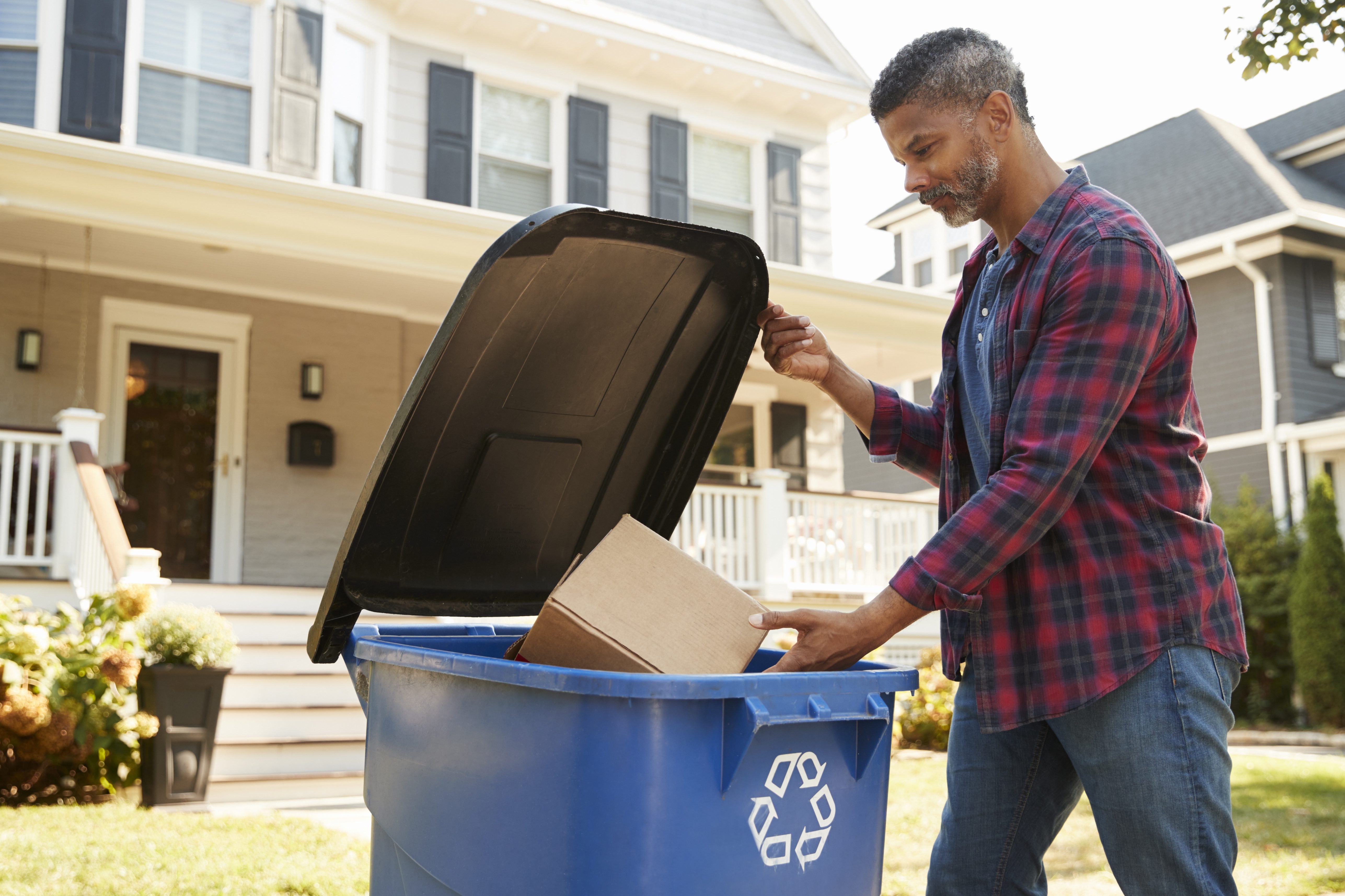 Homem jogando caixa em lixeira para materiais recicláveis