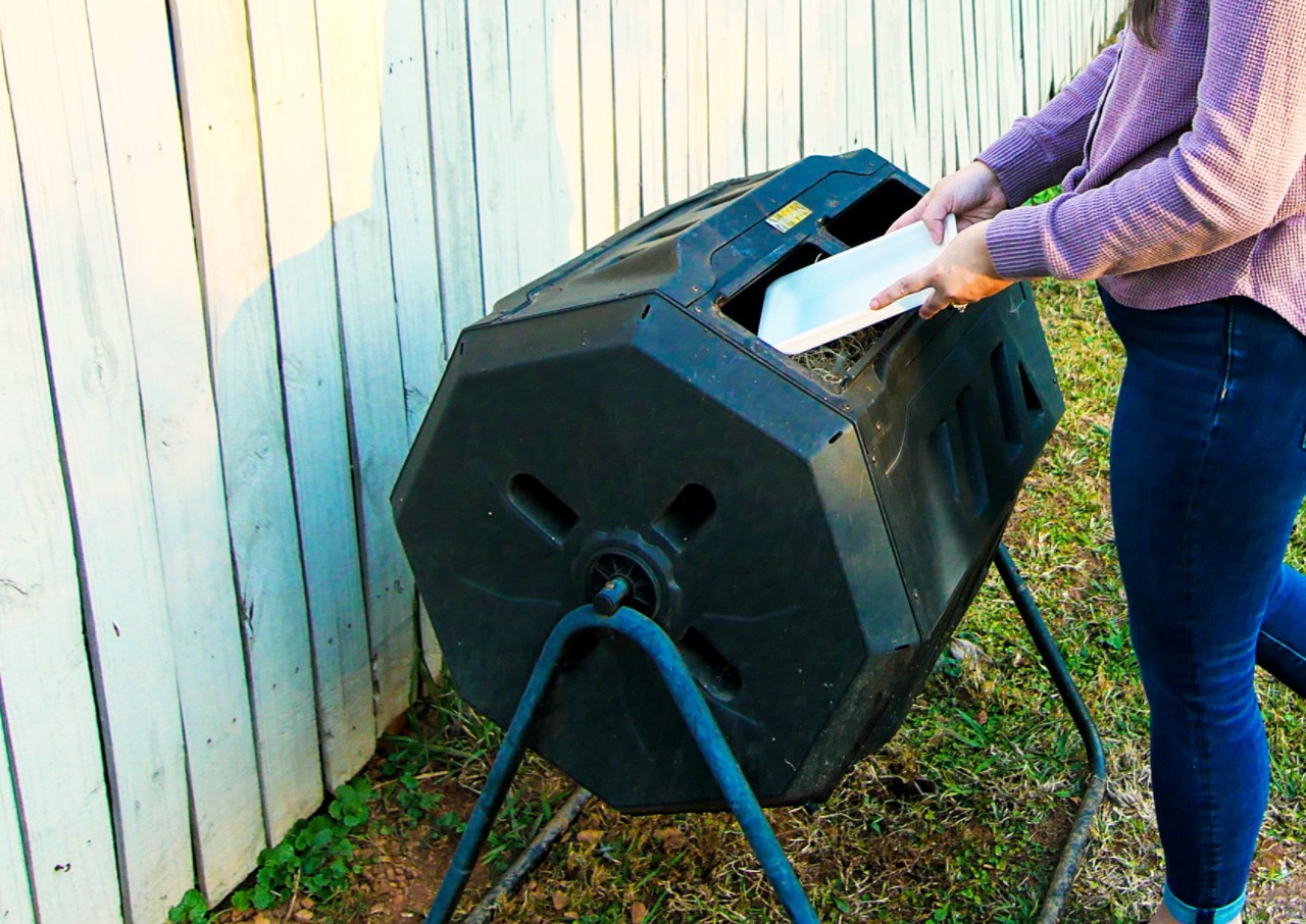 a woman putting a compostable tray in the compost tumbler