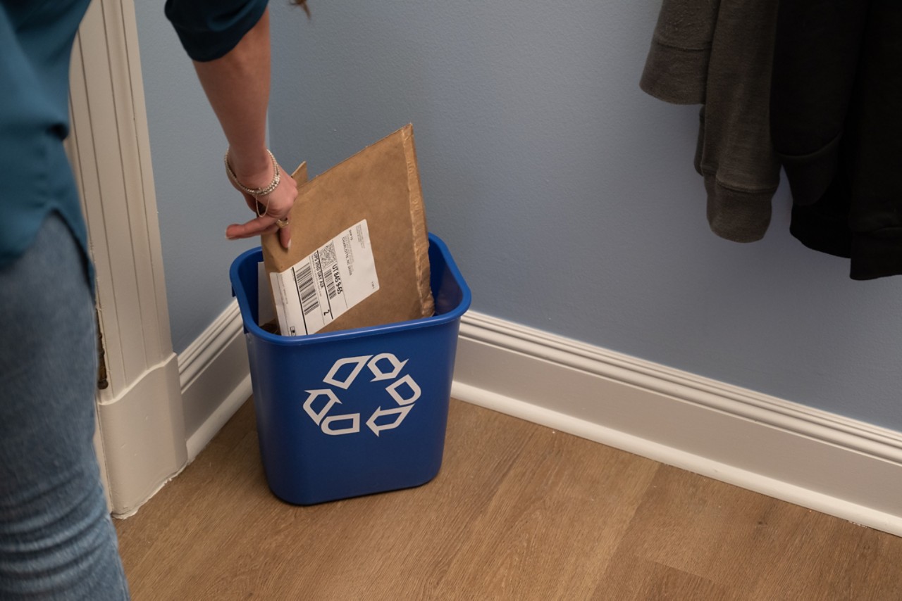 person placing paper bubble mailer into a recycle bin